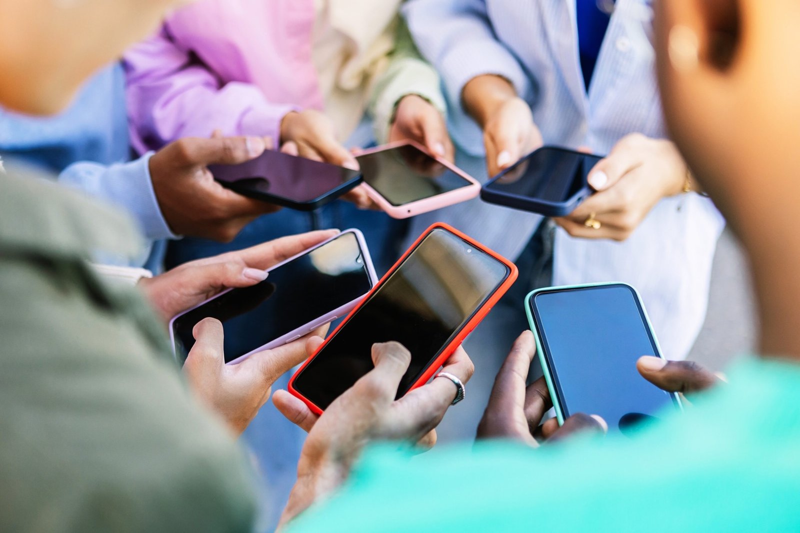 Photo: Young group of people standing in the circle using mobile phones outside.